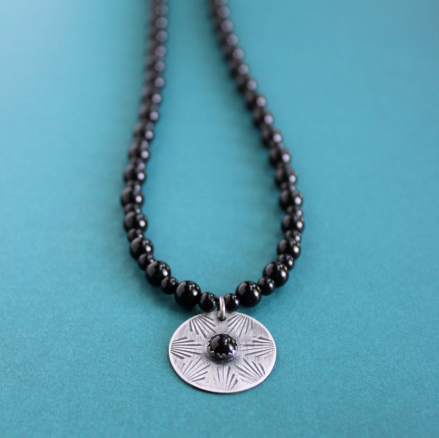 A men's necklace with polished black onyx stone beads and a sterling silver hand stamped disc pendant with an onyx cabochon.